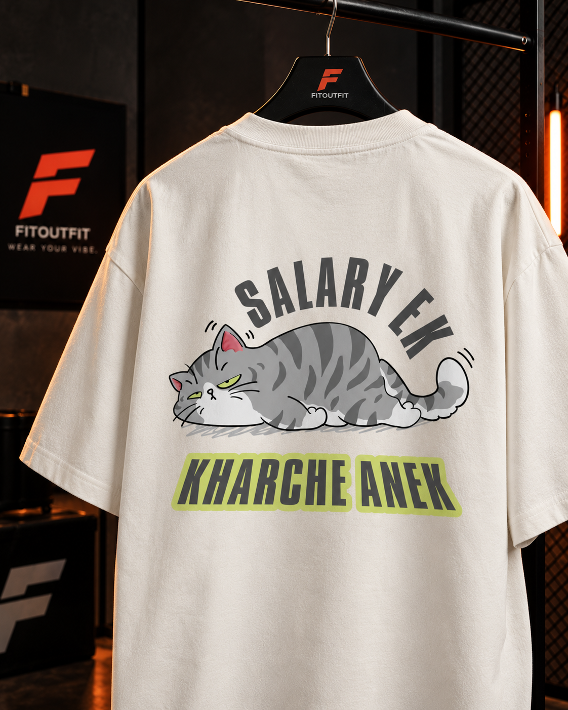 An off-white t-shirt hanging on a black hanger branded with the FitOutfit logo, showing the back of the shirt with a cartoon cat graphic and the text 'SALARY EK KHARCHE ANEK' in dark gray and green.
